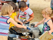 Several young children make muffins and cakes in the outdoor mud kitchen