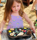 A young girl decorates the mud muffins with flowers and shells