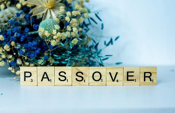 Wooden game tiles spelling out Passover in front of some flowers