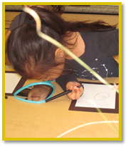 A child looking down at a small mirror and drawing her own face on a piece of paper