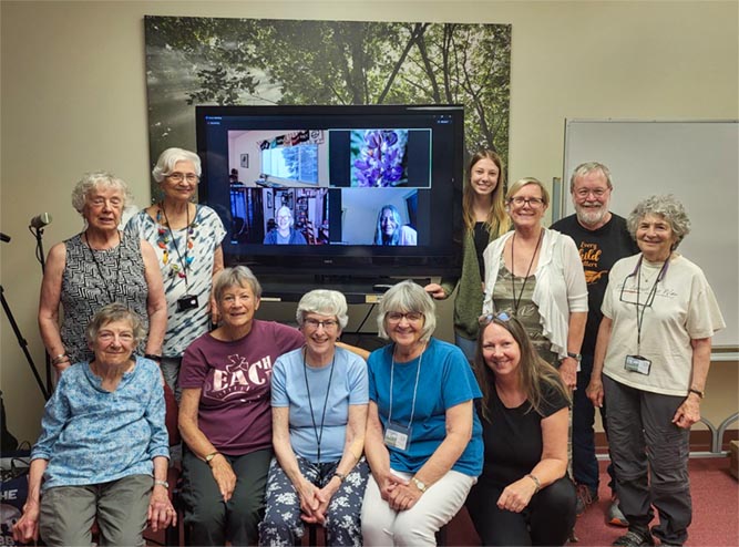A group of adults posing around a large video screen in a classroom.