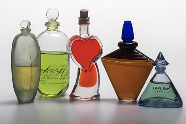 Four clear glass perfume bottles with colourful liquids inside, against a white background.