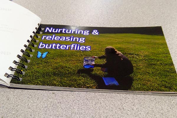 A spiral-bound book open to a photo page with text, "Nurturing and releasing butterflies"