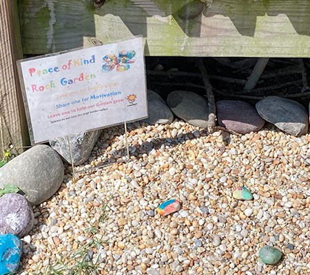 A small laminated sign reading Peace of Kind Rock Garden is placed in the corner of an area covered with pebbles.