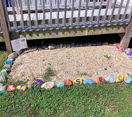 A small rock garden with pebbles in the center and larger painted rocks around it which spell out kindness rocks.