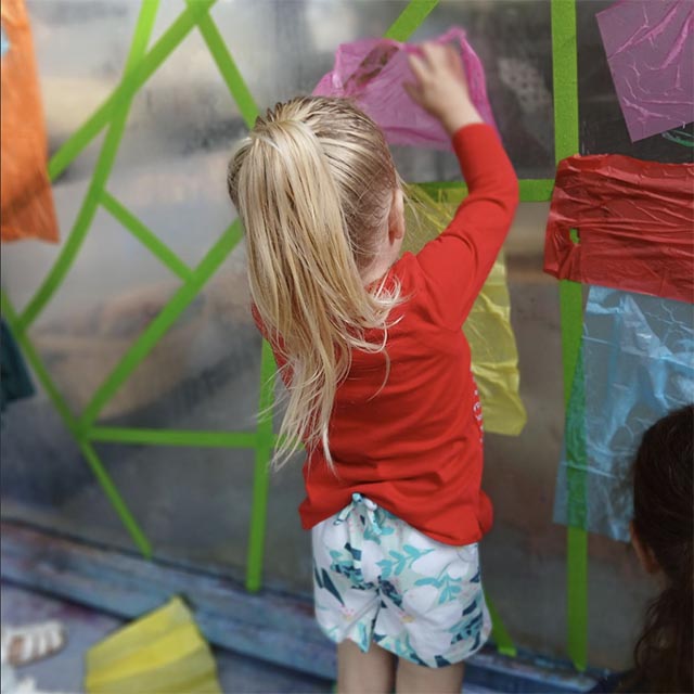 A young girl glues brightly colored tissue paper to a piece of plexiglass.