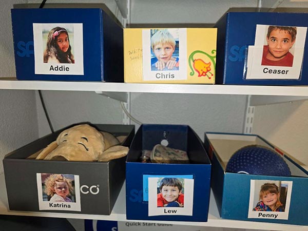 Shoeboxes on shelves, each box with a picture and name of a child.