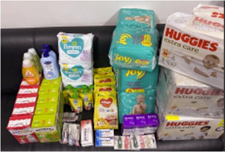 Packages of diapers, baby lotion, infant medicines and other baby supplies piled up against a wall.