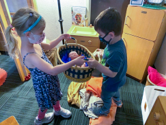 2 pre-k children hold a basket of toys as they clean up