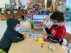 2 pre-k boys sit at a table in a classroom playing a board game